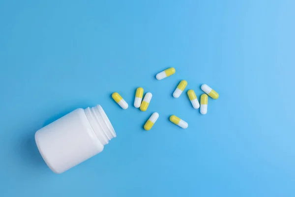 Pastillas blancas y amarillas, comprimidos y frasco blanco sobre fondo azul — Foto de Stock