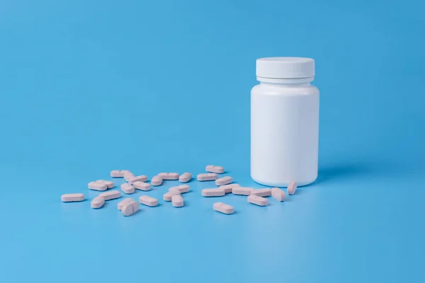 Pillole rosa, compresse e bottiglia bianca su sfondo blu — Foto Stock