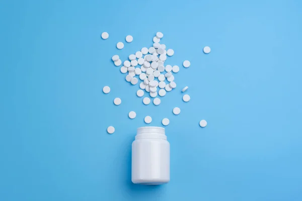 Pillole bianche, compresse e bottiglia bianca su sfondo blu — Foto Stock
