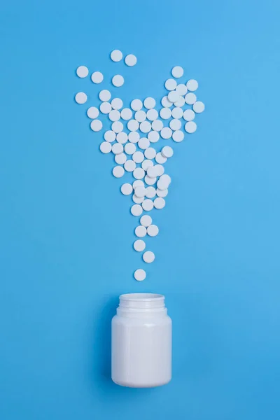 Pastillas blancas, tabletas y frasco blanco sobre fondo azul — Foto de Stock