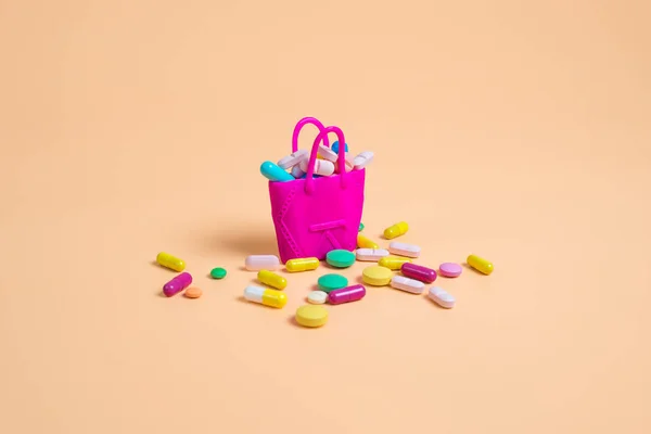 Pílulas coloridas caem de uma bolsa rosa em um fundo laranja — Fotografia de Stock