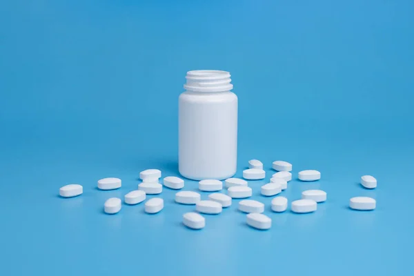 Pastillas blancas, tabletas y frasco blanco sobre fondo azul — Foto de Stock