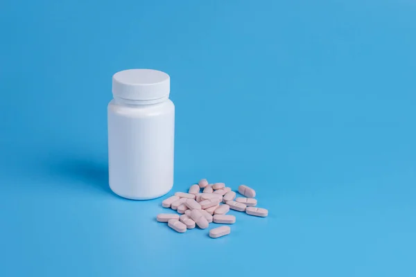 Pastillas rosadas, tabletas y frasco blanco sobre fondo azul — Foto de Stock