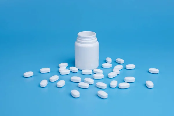 Pastillas blancas, tabletas y frasco blanco sobre fondo azul — Foto de Stock