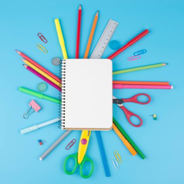 Renkli okul malzemeleri ve notepadon mavi bir arka plan.