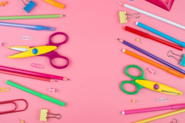 Pembe arka plan üzerine bir kağıt üzerinde renkli okul malzemeleri