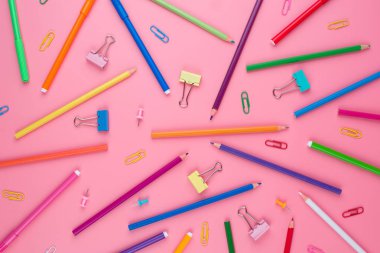 Pembe arka plan üzerine bir kağıt üzerinde renkli okul malzemeleri.
