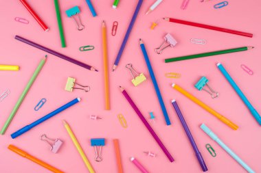 Pembe arka plan üzerine bir kağıt üzerinde renkli okul malzemeleri.