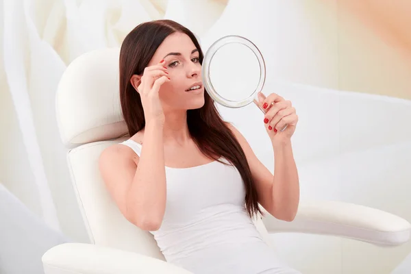Cosmetic treatments in a professional cosmetic clinic - a young woman looks at her face in the mirror