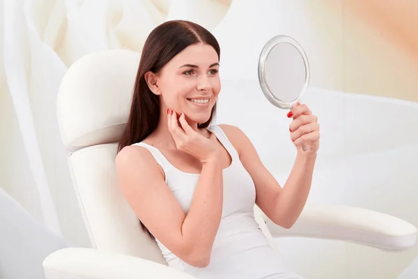 Cosmetic treatments in a professional cosmetic clinic - a young woman looks at her face in the mirror