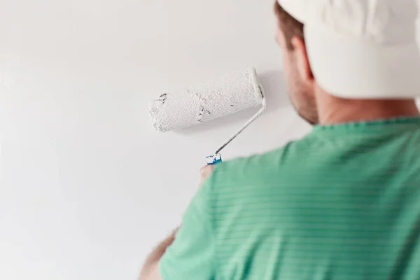 Giovane uomo che dipinge un muro sul bianco in una casa moderna — Foto Stock