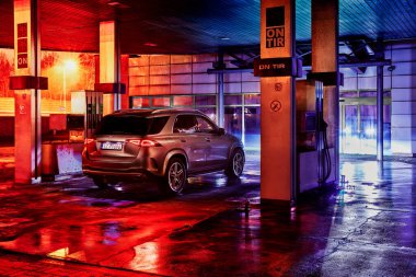 Katowice / Polonya - 01 / 11 / 2020: Terk edilmiş bir benzin istasyonunda duran lüks Mercedes GLE. Her şey, ıslak asfalta yansıyan renkli şehir ışıklarıyla aydınlatılıyor. Motor V6, 367 HP