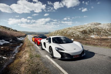 Rjukan / Norway -04.06.2016: White Mclaren 650s, Red Ferrari f12 and Yellow Lamborghini Huracan. Three super cars stopped for a while in a journey through the mountains of Norway in an empty valley. clipart