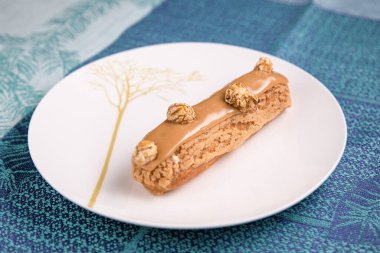 Beyaz tabakta karamel jöleli ekler var. Tabağın altında turkuaz masa örtüsü.