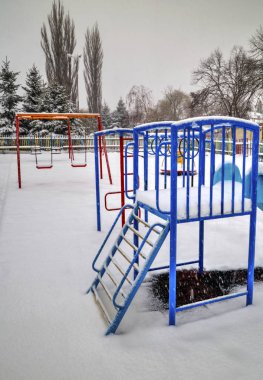 Çocuk parkı kışın karla kaplı.