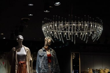 iki göz alıcı mankenler giysileri ile rafların arka planda parlak bir vintage pahalı avize ışığı altında bir giyim mağazasında duruyor