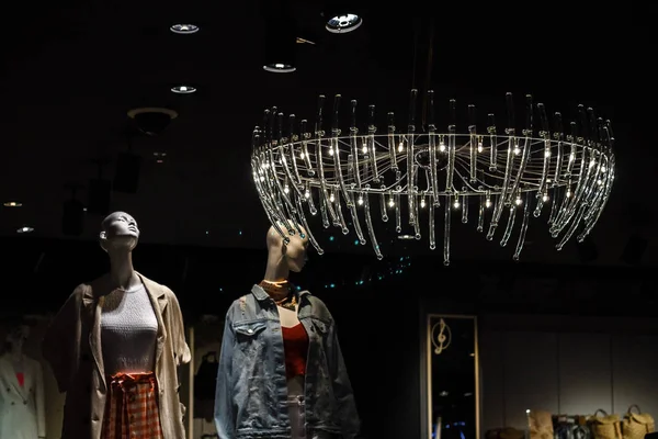 iki göz alıcı mankenler giysileri ile rafların arka planda parlak bir vintage pahalı avize ışığı altında bir giyim mağazasında duruyor