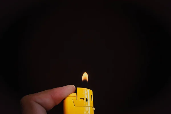 人的手在他的手指上拿着一个黄色的打火机 并点亮它 火焰形成在黑色背景 — 图库照片