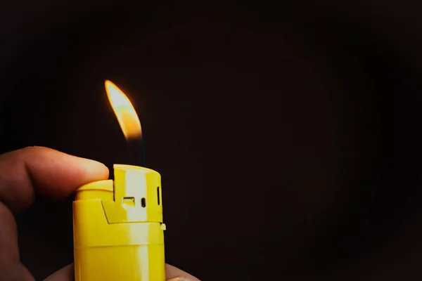 insan eli parmaklarında sarı bir çakmak tutar ve ışıklar; siyah bir arka plan üzerinde oluşan alev