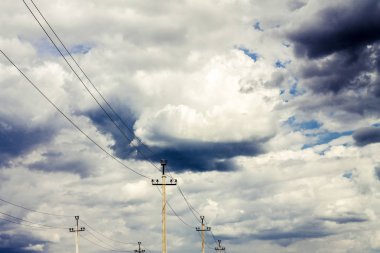kalın bulutlar ile gökyüzüne karşı aralarında yüksek gerilim telleri ve kutuplar vardır