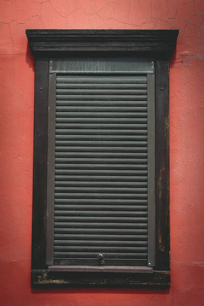 brown shutters on a wooden window on a light burgundy wall; vertical orientation of the photo
