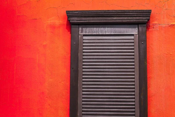 brown shutters on a wooden window on a wall painted in bright red-orange color