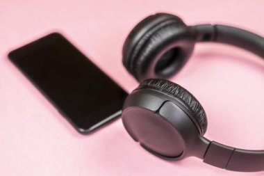 Pembe arka planda kulaklıklı akıllı telefonun yakın çekim. (Üstgörünüm). Müzik dinleyin. 