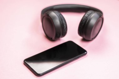 Pembe arka planda kulaklıklı akıllı telefonun yakın çekim. (Üstgörünüm). Müzik dinleyin. 