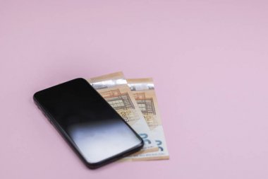 Pembe arka planda para ile akıllı telefon yakın çekim. (Üstgörünüm). Müzik dinleyin. 