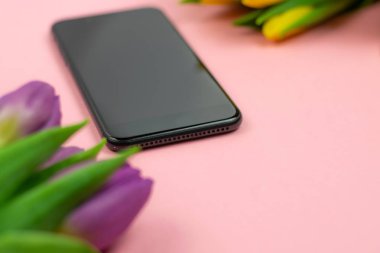 Pembe arka planda mor ve sarı laleler ve siyah akıllı telefon buketi. Üst te. Kopya alanı. Sunu şablonu.