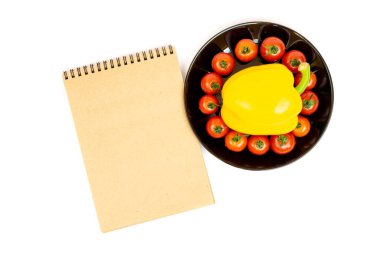 Yellow sweet pepper with tomatoes in a black plate isolated on white background near Notepad. Composition of yellow peppers and red tomatoes on a white background. Place for your text
