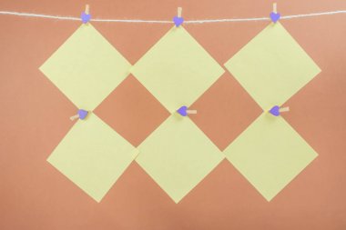 Çamaşır ipinde sarı çıkartmalar ve kahverengi arka planda izole edilmiş mandallar. Metnin için yer.