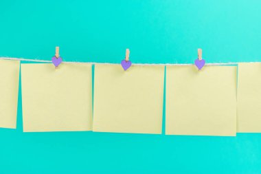 Mavi arka planda izole edilmiş çamaşır iğneleri ile çamaşır ipinde yeşil çıkartmalar. Metniniz için yer.