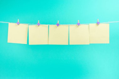 Mavi arka planda izole edilmiş çamaşır iğneleri ile çamaşır ipinde yeşil çıkartmalar. Metniniz için yer.