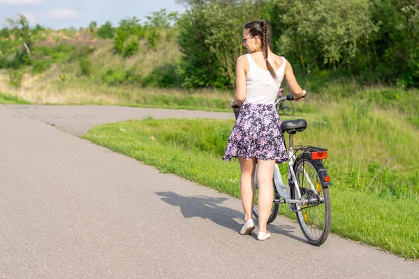 Active life. A woman with a bike enjoys the view at summer forest. Bicycle and ecology lifestyle concept.