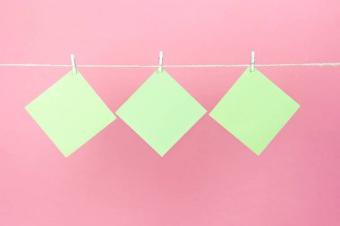 Çamaşır ipinde sarı çıkartmalar ve pembe arka planda izole edilmiş mandallar. Metnin için yer.