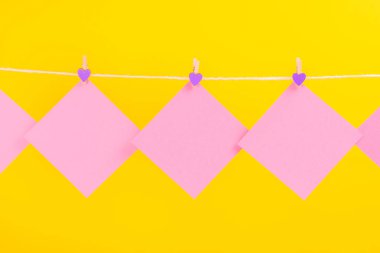 Sarı arka planda izole clothespins ile clothesline üzerinde pembe çıkartmalar. Metniniz için yer.