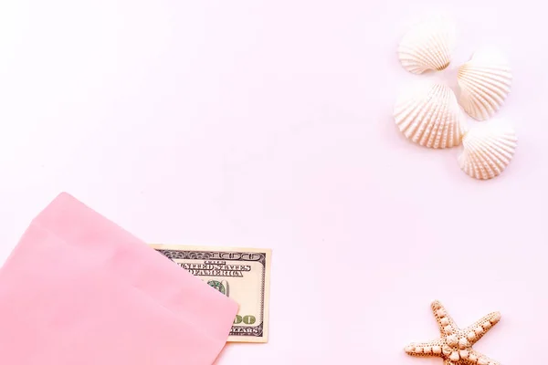Money in a pink envelope, starfish, seashells on a pink background. Concept: Money for rest