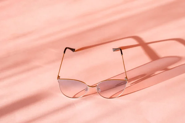 Eine rosafarbene Sonnenbrille mit Metallrahmen wirft einen Schatten auf die rosa Oberfläche. — Stockfoto