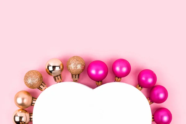 Christmas pink and gold balls with gift box on pink. Christmas gifts and decoration on white background with copy space for text. Holiday and celebration concept for postcard or invitation. Top view