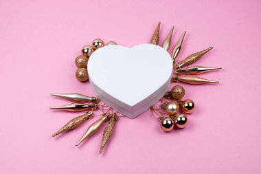 Kalp şeklinde Noel hediye kutusu, pembe bir arka planda Noel topları. Dalga geçme. Noel kompozisyon.