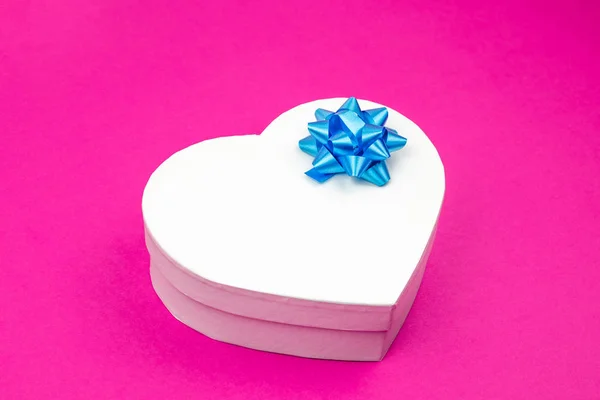 Heart shaped gift box with blue bow on a pink background. Mock up. Empty place for an inscription. Present for the christmas, thanks giving day, birthday holiday.