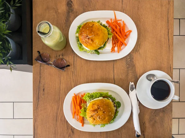 Velsmakende hjemmelagde hamburgere med biff, gulrøtter, ost, salat og kaffe, cocktail på trebord . – stockfoto