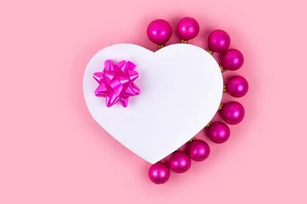 Gift box, pink bow, christmas balls on pink background. Holiday and celebration concept for postcard or invitation. Top view