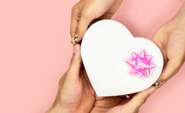 Sarı arka plan Düz yatıyordu pembe yay ile şekil kalp hediye kutusu tutan erkek ve kadın ellerin üst görünümü. Doğum günü, sevgililer günü, Noel, Yeni Yıl için hediye. 