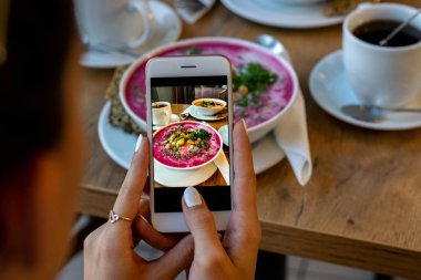 Smartphone gıda fotoğraf kase havuç çorbası. Kadın elleri sosyal ağlar için akşam yemeği veya öğle yemeği telefon fotoğrafı çekmek. Çiğ vegan vejetaryen sağlıklı gıda