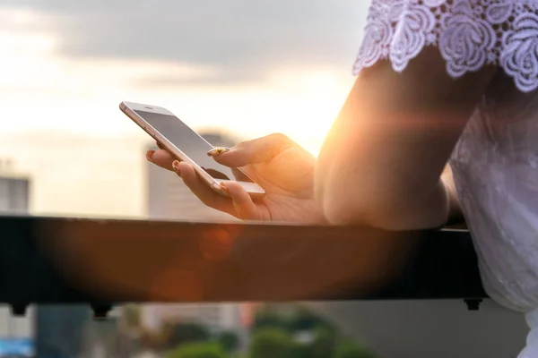 Wanita mengetik pesan tertulis di smartphone saat matahari terbenam. Foto gadis muda cantik dengan smartphone . — Stok Foto