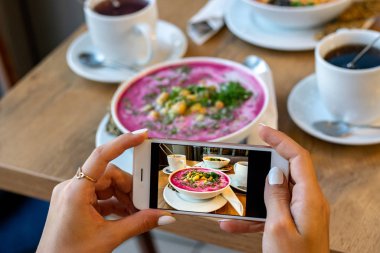 Smartphone gıda fotoğraf kase havuç çorbası. Kadın elleri sosyal ağlar için akşam yemeği veya öğle yemeği telefon fotoğrafı çekmek. Çiğ vegan vejetaryen sağlıklı gıda