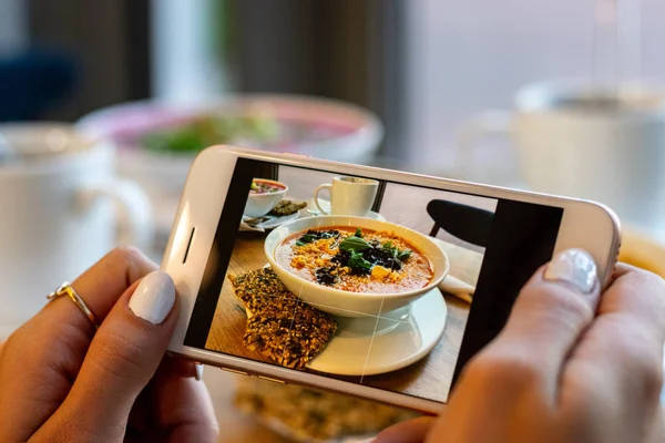 Unge kvinde hænder gøre foto af græskar og gulerod suppe. Tag sociale netværk smartphone mad fotografering. Rå vegansk vegetarisk sund mad - Stock-foto