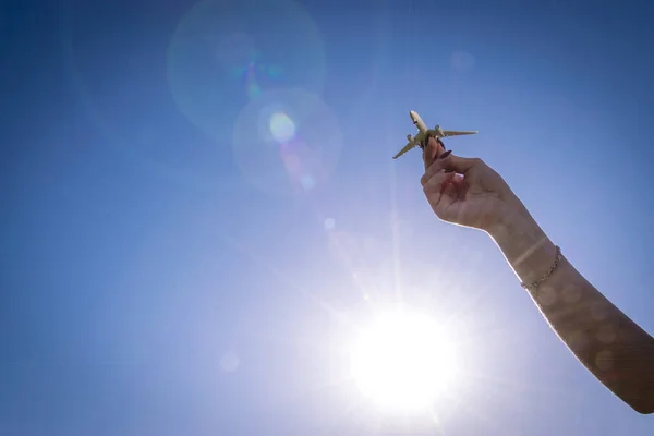 子供の手に高い飛行機の白いおもちゃは、太陽の光の空を飛ぶ。飛行機のフライト、航空機の明るい太陽の下での旅行の背景。空気概念. — ストック写真